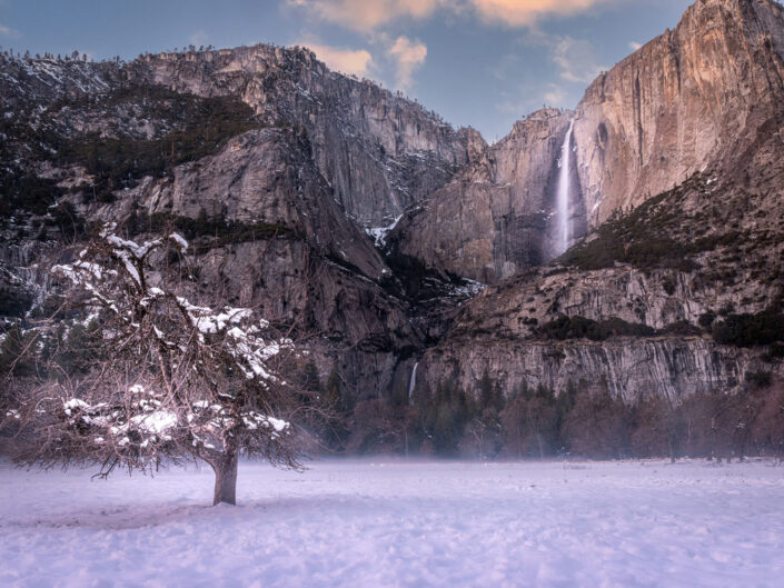Yosemite Falls in winter, framed by icicles and snow-covered cliffs.